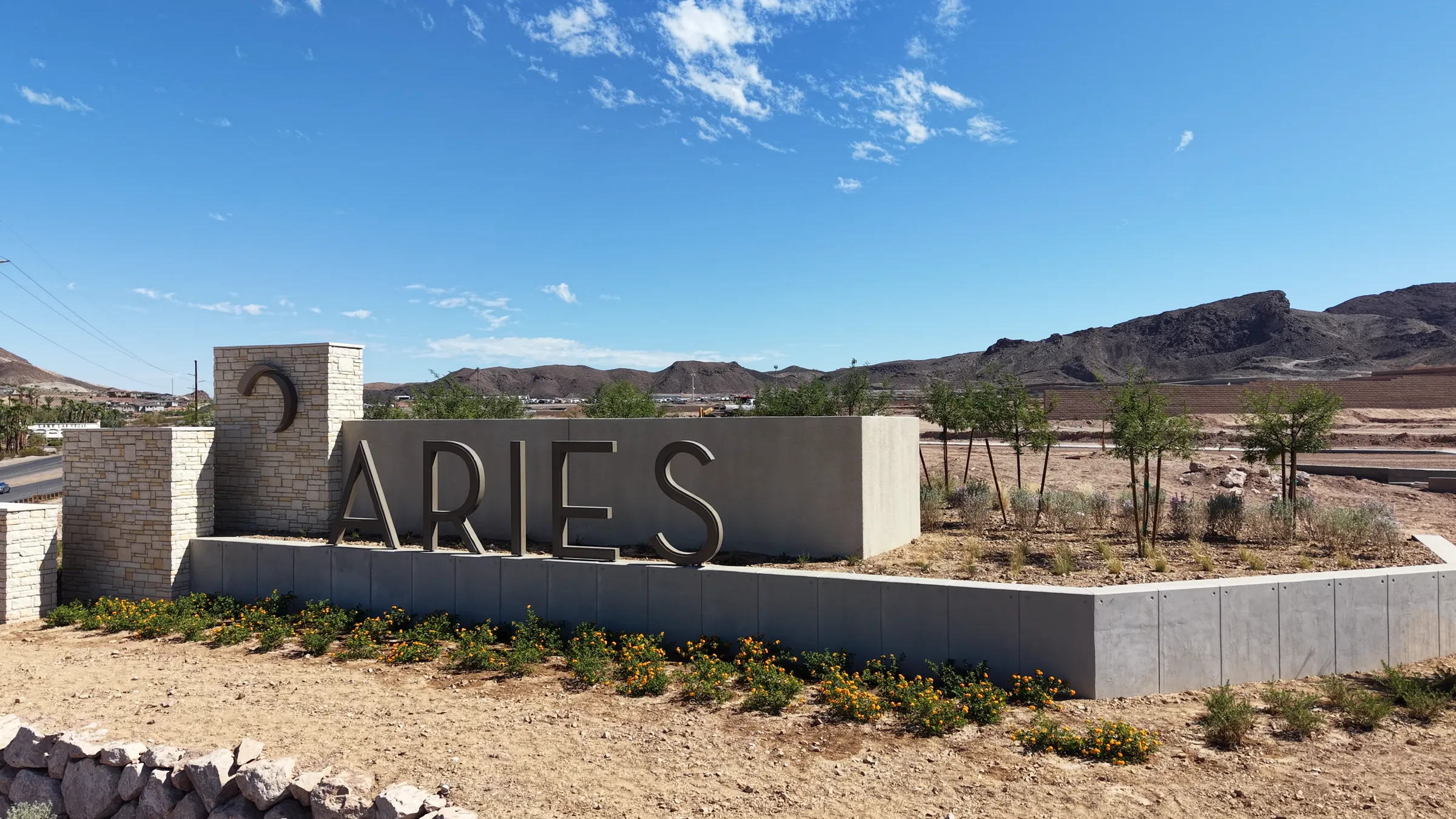 The Aries monument sign at the community entrance in east Henderson, with new landscaping in front and desert mountains behind it under a blue sky.